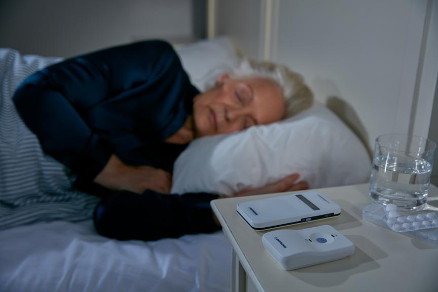 Elderly woman laying in bed hard moniroring devices on the nightstand