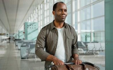 Na foto, homem negro empurra carrinho de bagagem pelo corredor do aeroporto