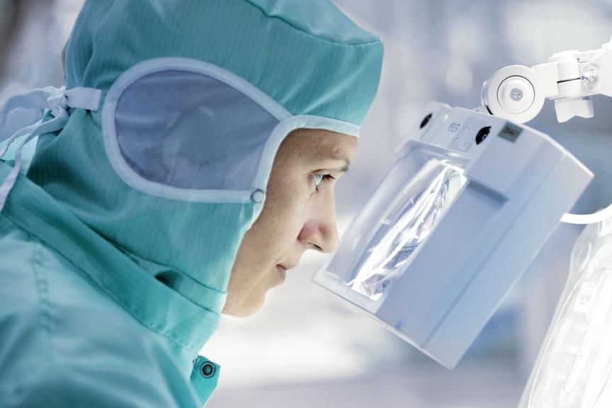 Woman looking through magnifying glass wearing sterile gear in lab