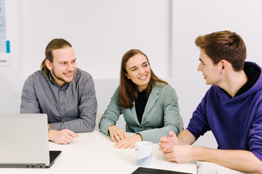 three people sitting in front of a laptop and talking