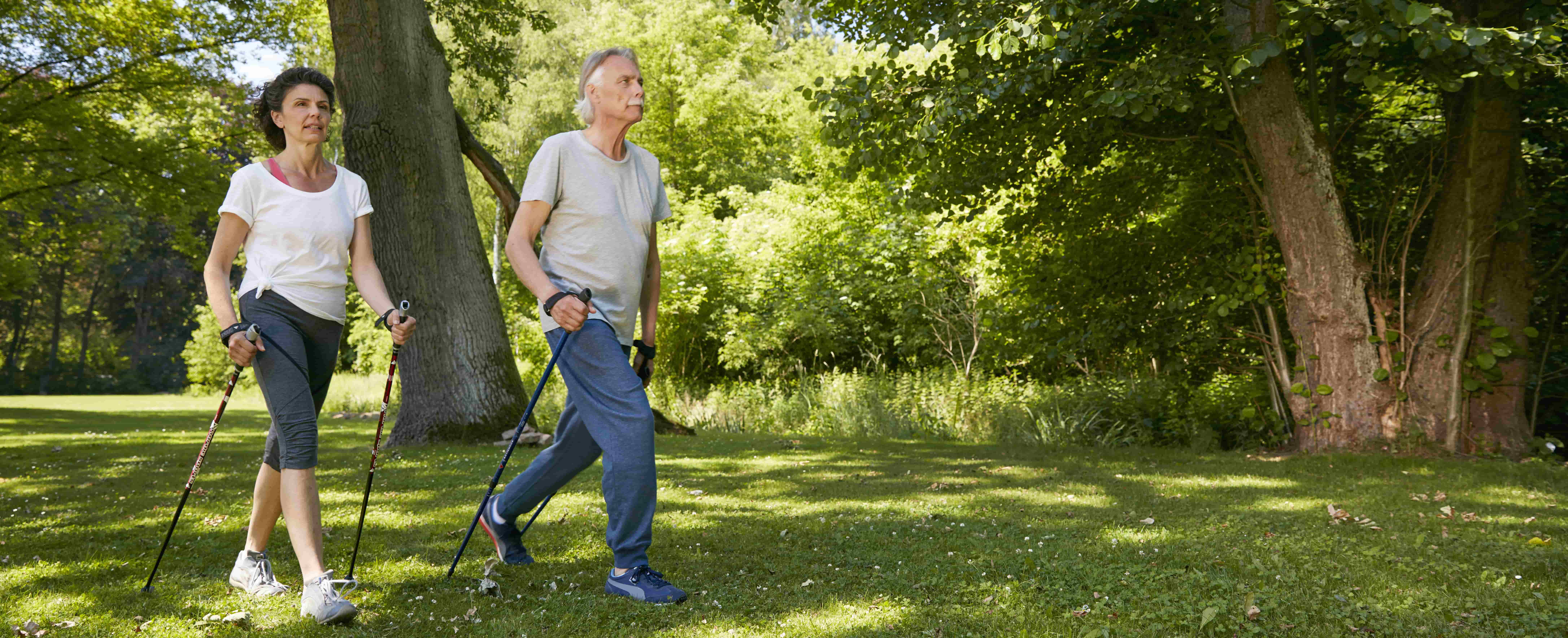 Foto de um casal de meia idade no parque durante o dia usando um par de bastões cada para ajudar na caminhada