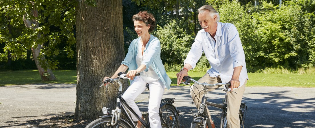 Foto de uma mulher e um homem de meia-idade andando de bicicleta durante o dia em um parque arborizado 