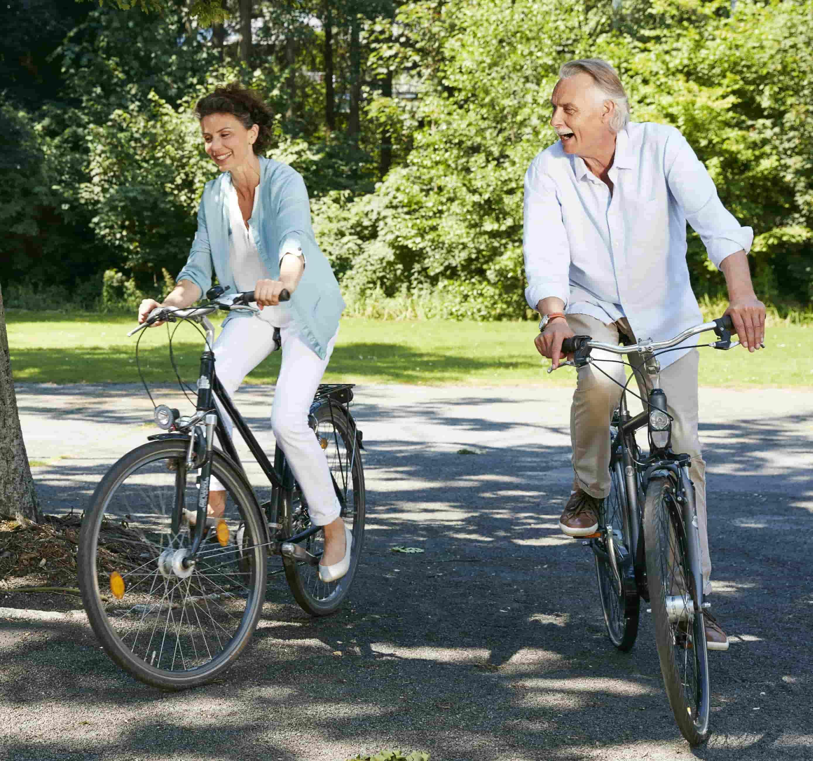 Foto de uma casal de meia-idade andando de bicicleta em um local com muitas árvores