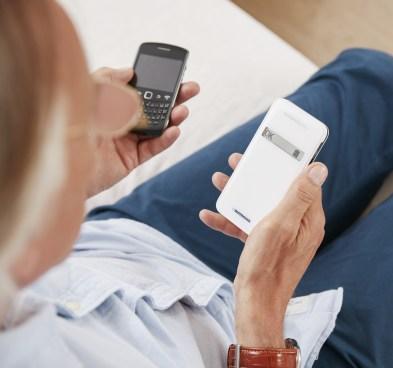 Foto de cima para baixo de um homem de meia-idade sentado segurando com uma mão um dispositivo CardioMessenger e com a outra mão um celular 